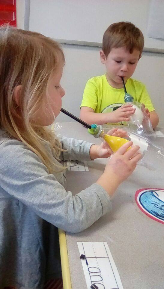 Two children blowing into bottles with straws and balloons attached