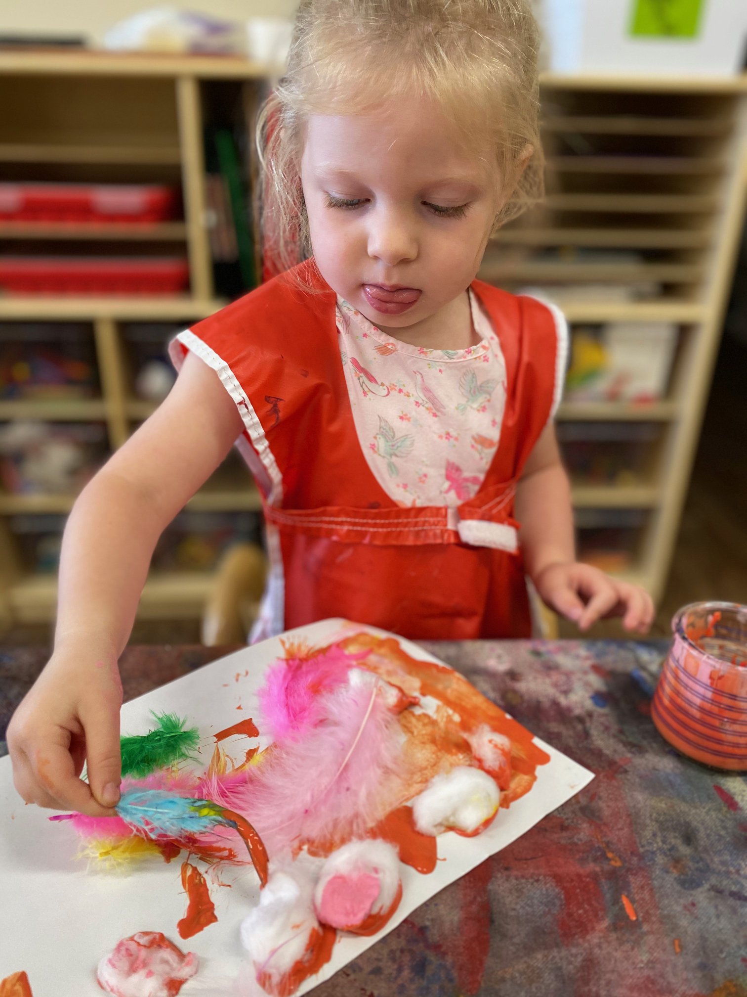 Child in a red smock adding feathers to a painting