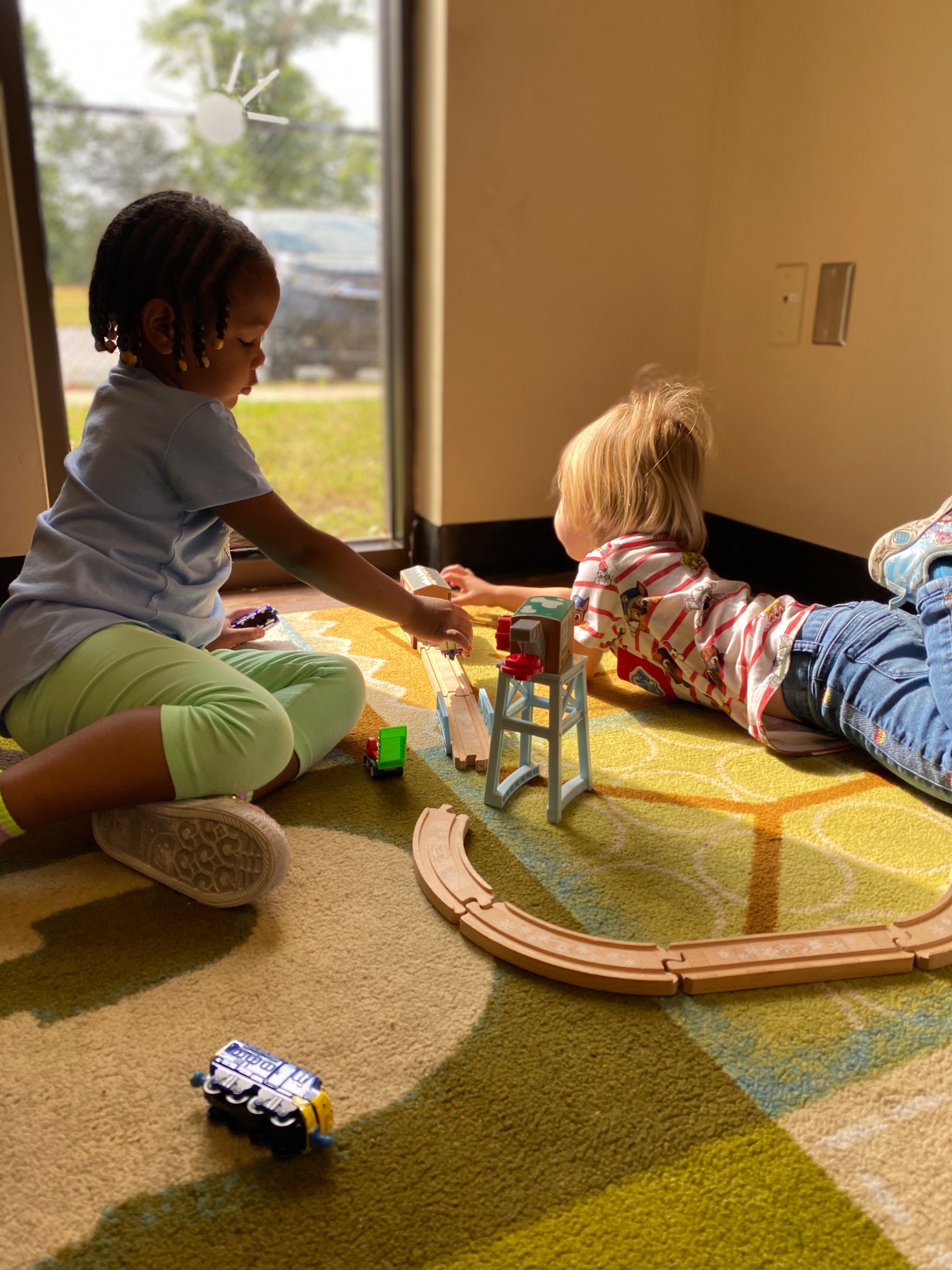 Two children playing with a toy train set on a carpeted floor