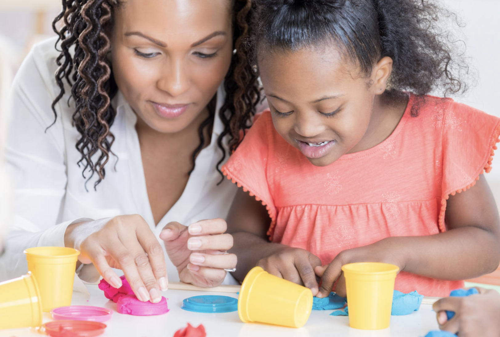 Person and child playing with colorful modeling clay and cups
