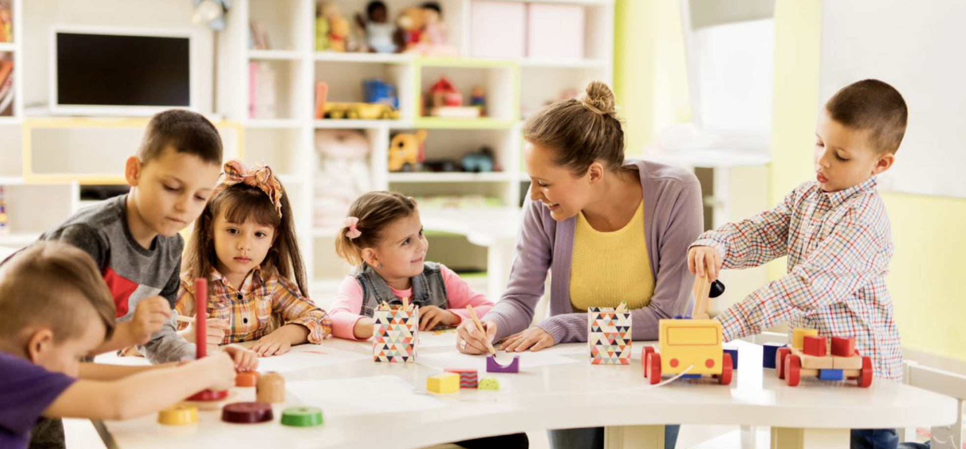 Adult and children playing with blocks and toys at a table