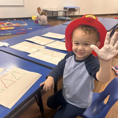 Child in a red hat with a white handprint on their palm, waving