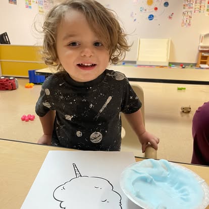 Child at a table with a unicorn drawing and blue paint