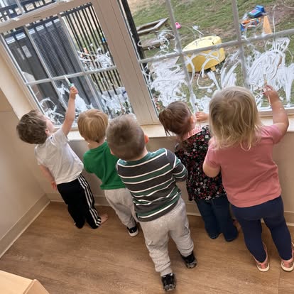Five children drawing on a window with white paint