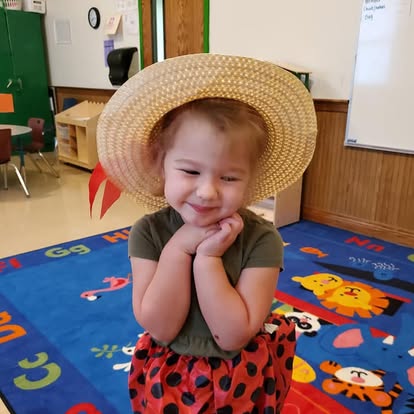 Child in a straw hat and polka dot skirt in a classroom