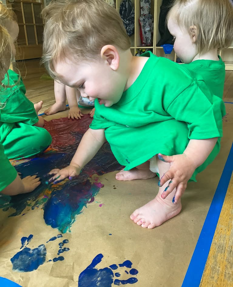 Children wearing green shirts finger painting on paper
