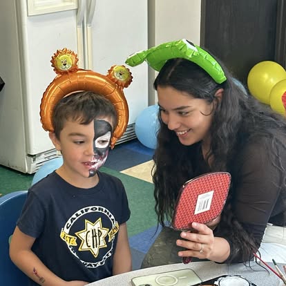 Person holding mirror for child with face paint and balloon headband