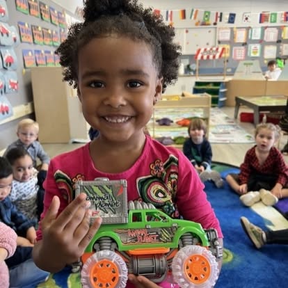 Child holding a toy monster truck in a classroom