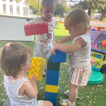 Three children playing with large building blocks outdoors