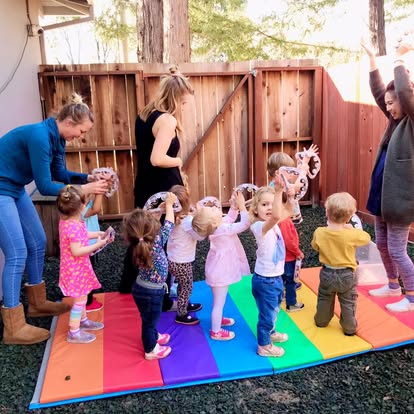 Adults and children playing with hoops on a rainbow mat outdoors