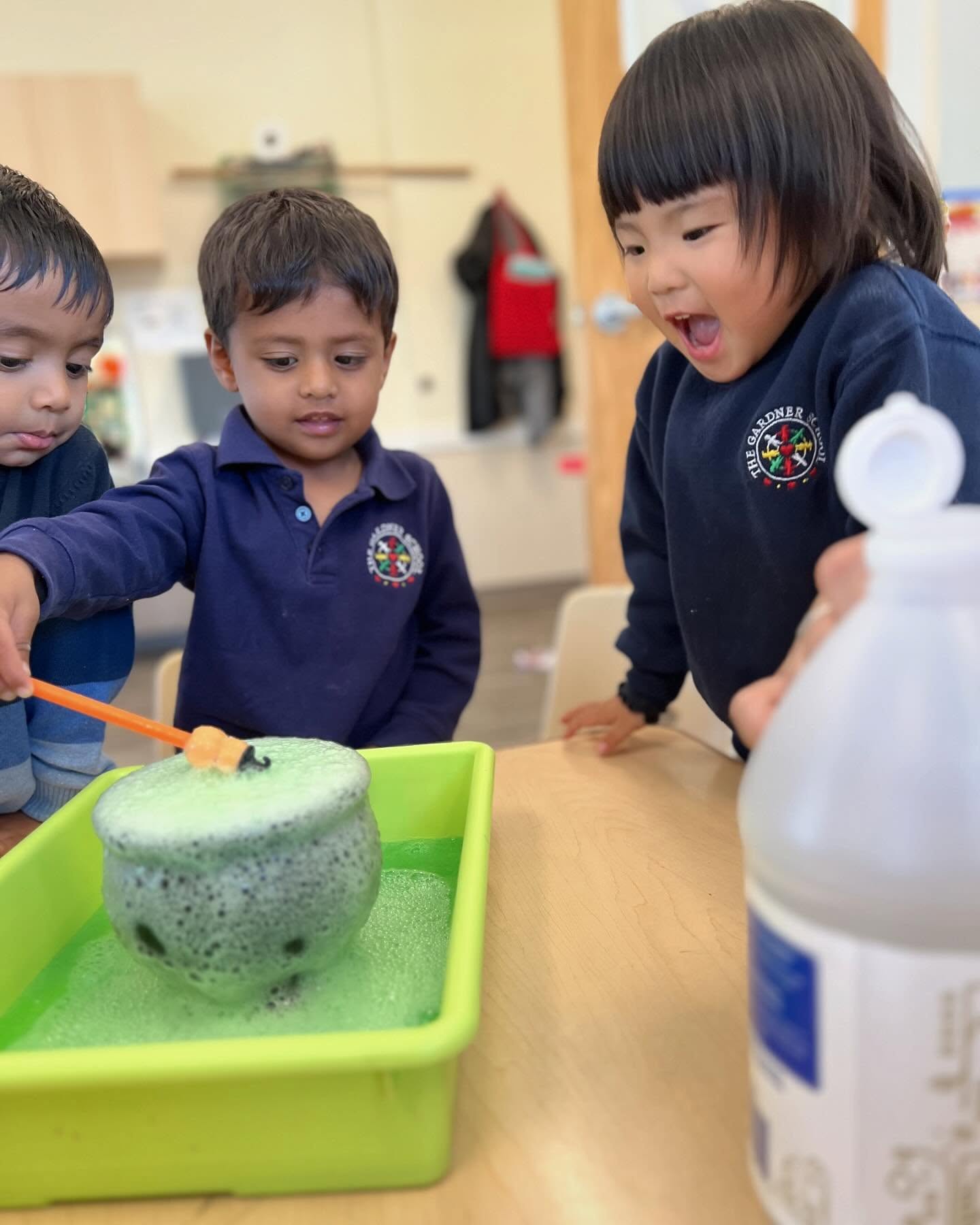 Three children watching green bubbles overflow from a pot