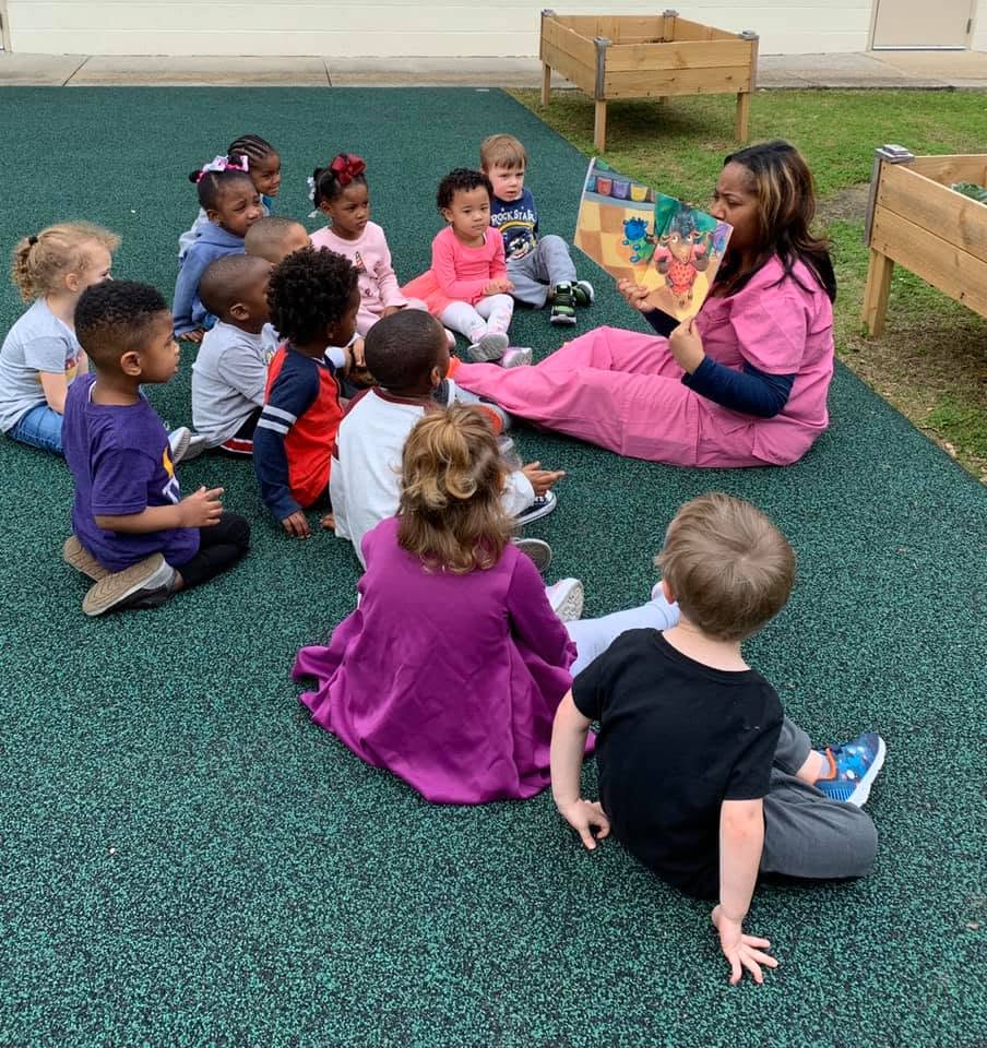Adult reading a book to a group of children sitting outside