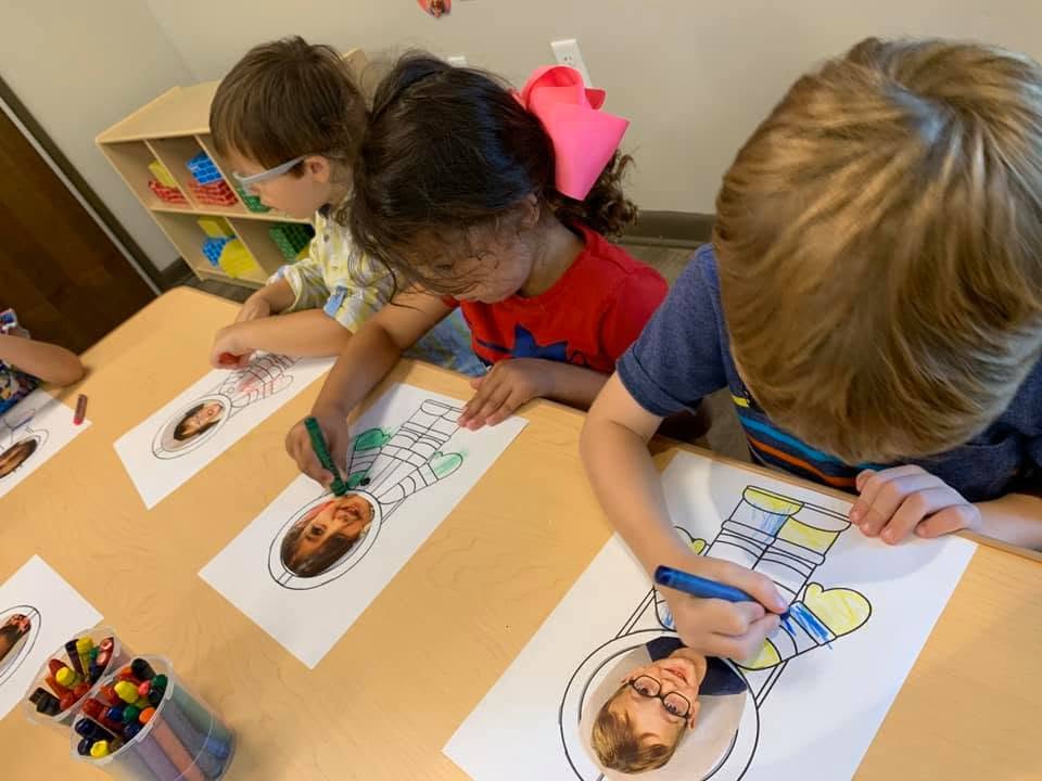 Children coloring astronaut drawings with paper photos of their faces