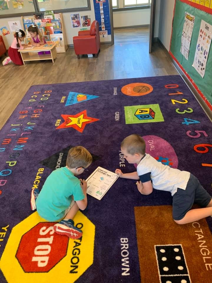 Two children lying on a classroom floor rug looking at a worksheet