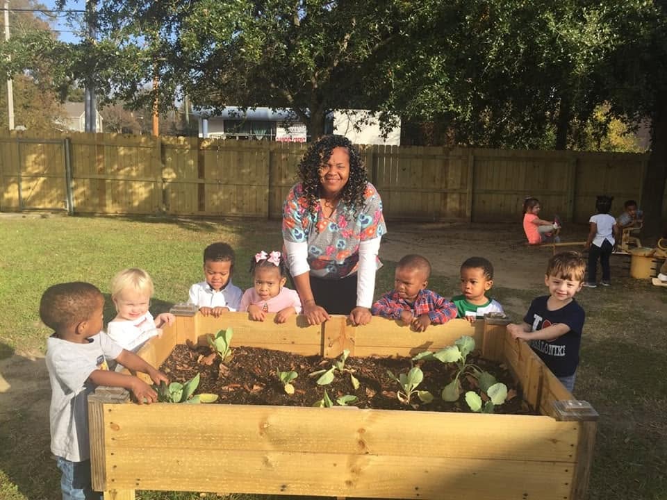 Adult and group of children gardening around a raised bed