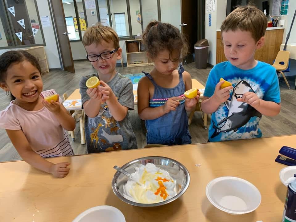 Four children holding lemon wedges while making a mixture in a bowl