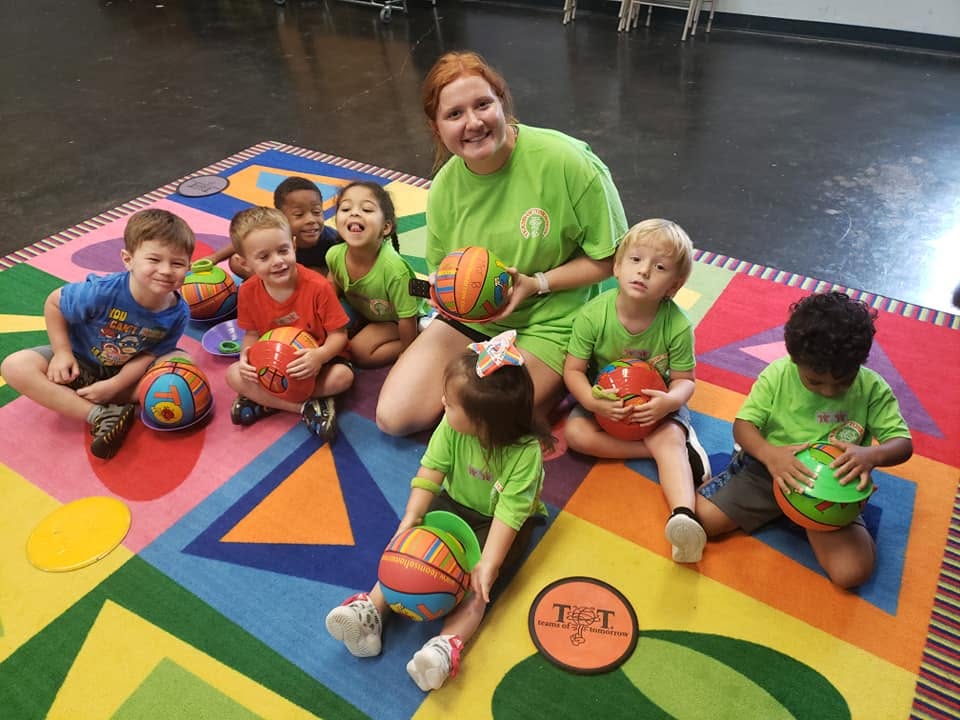 A group of children and an adult sitting on a colorful floor mat with toy balls