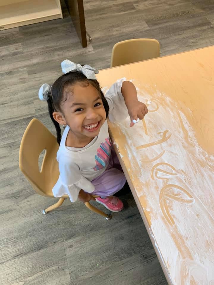 Child sitting at a table and drawing in powder