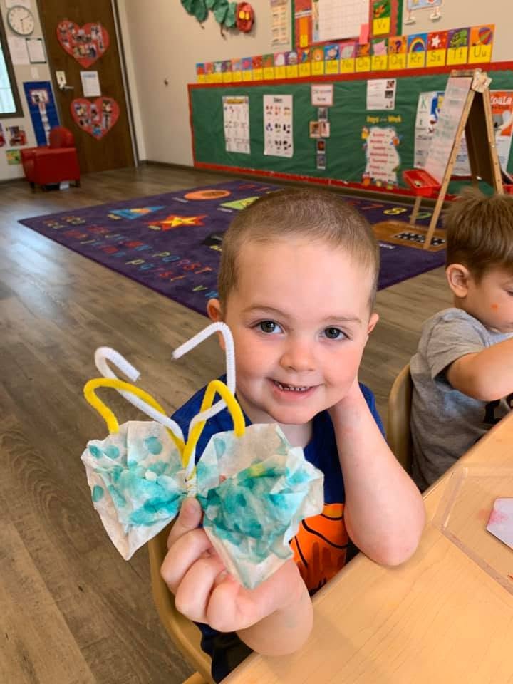 Child holding a butterfly craft made from a coffee filter in a classroom