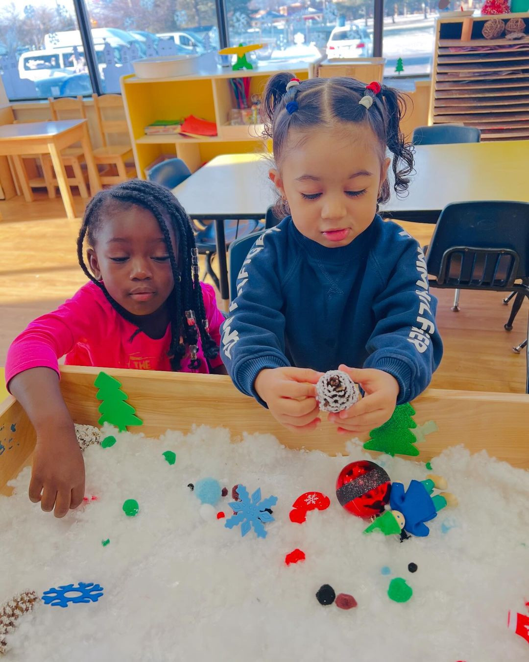 Two children playing with objects in a sensory bin filled with white material