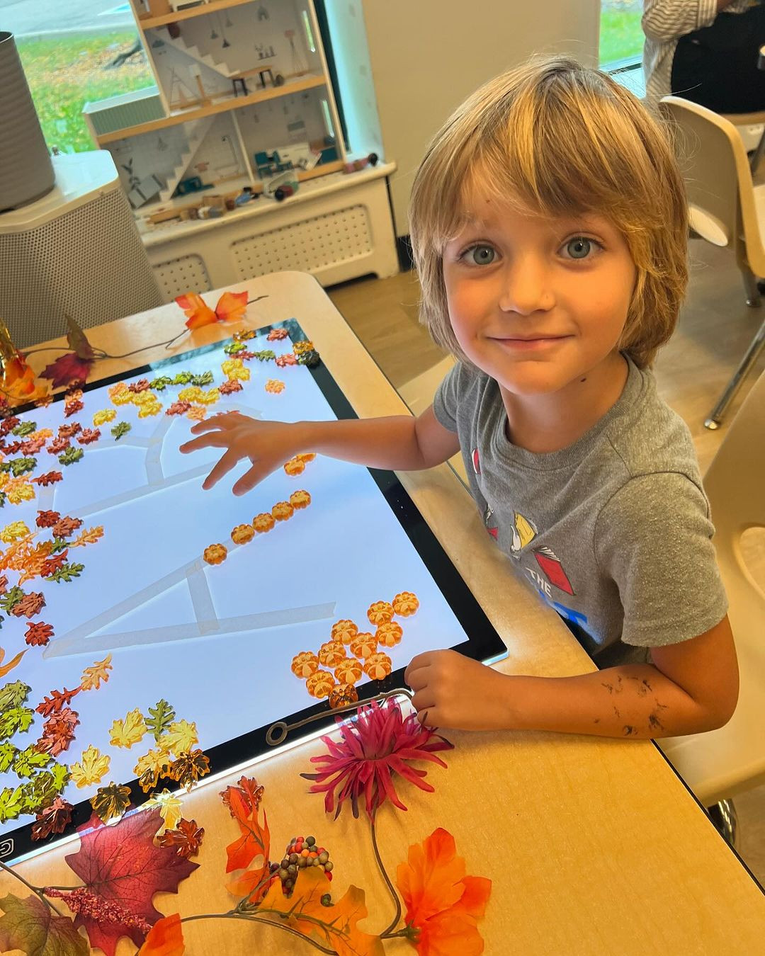 Child playing with fall-themed items on a light table