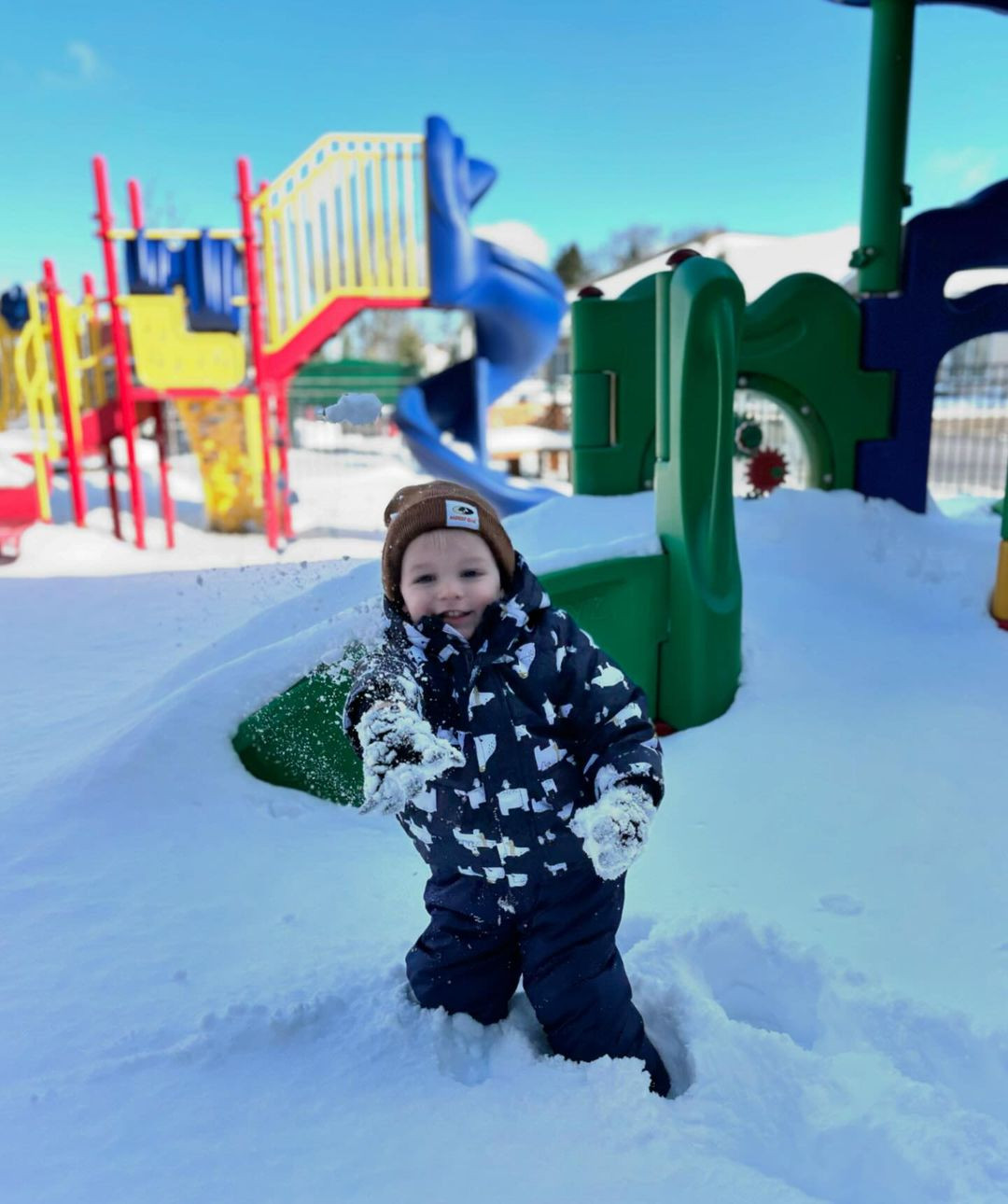 Child in winter clothing standing in snow at a playground