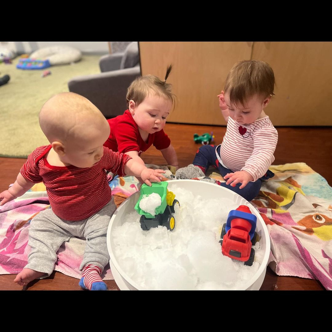 Three children playing with toy trucks in a white bin