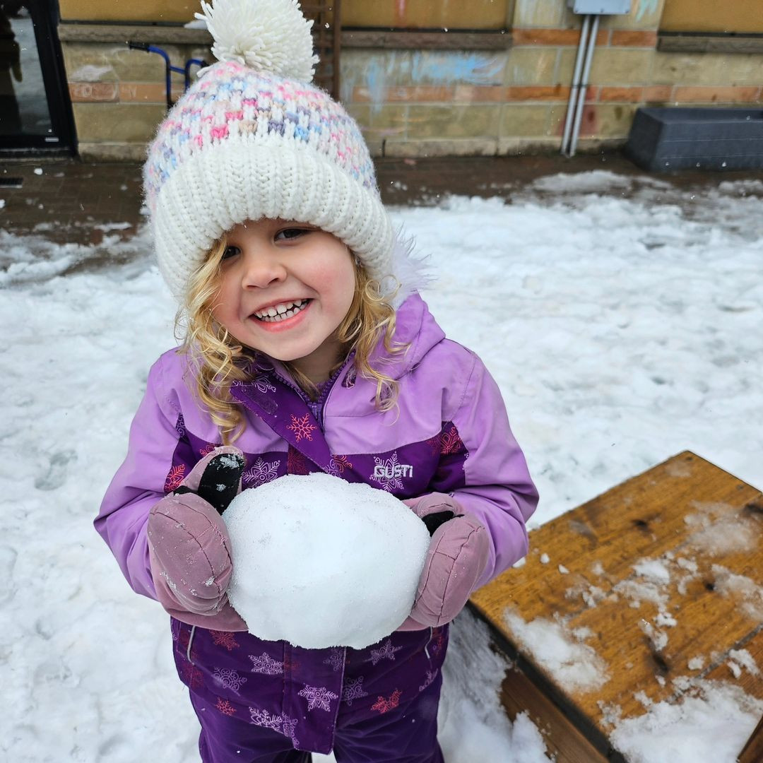 Child in winter clothing holding a snowball