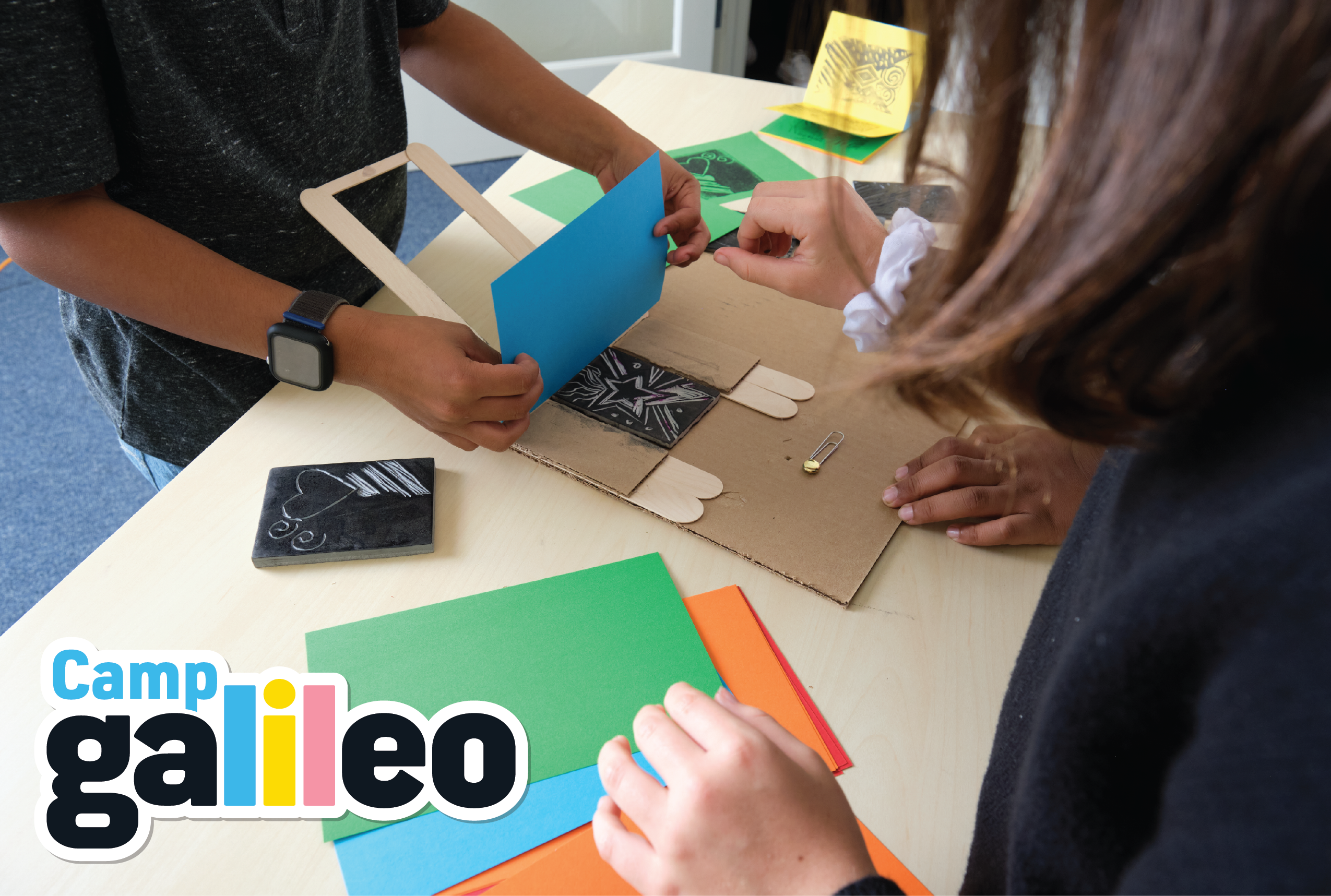 Two people working on a craft project with cardboard and colored paper