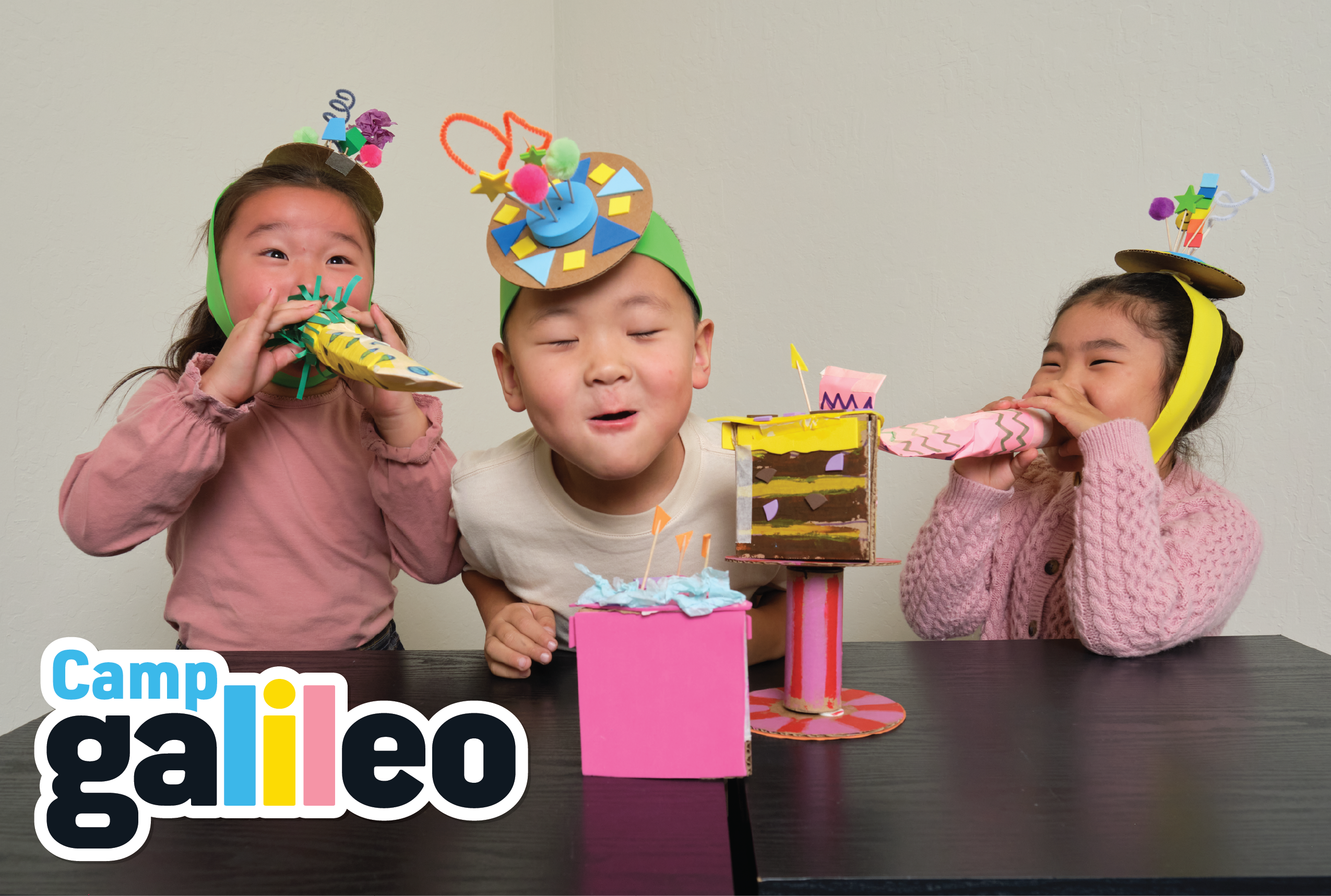 Three children with party hats and blowers around a craft cake