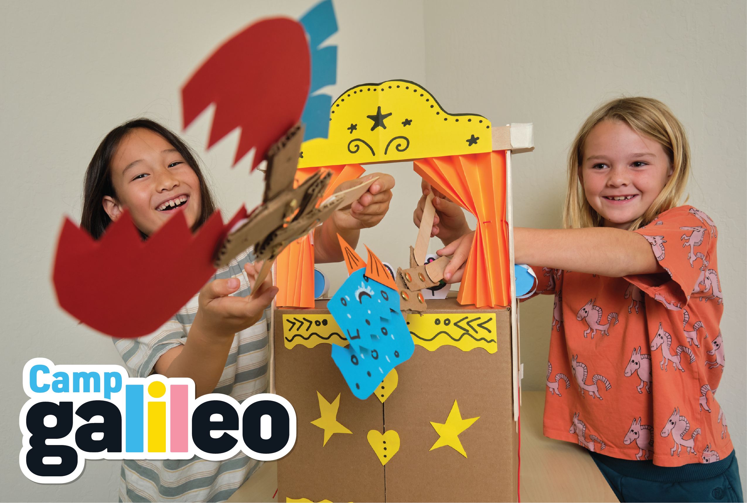 Two children playing with a cardboard puppet theater