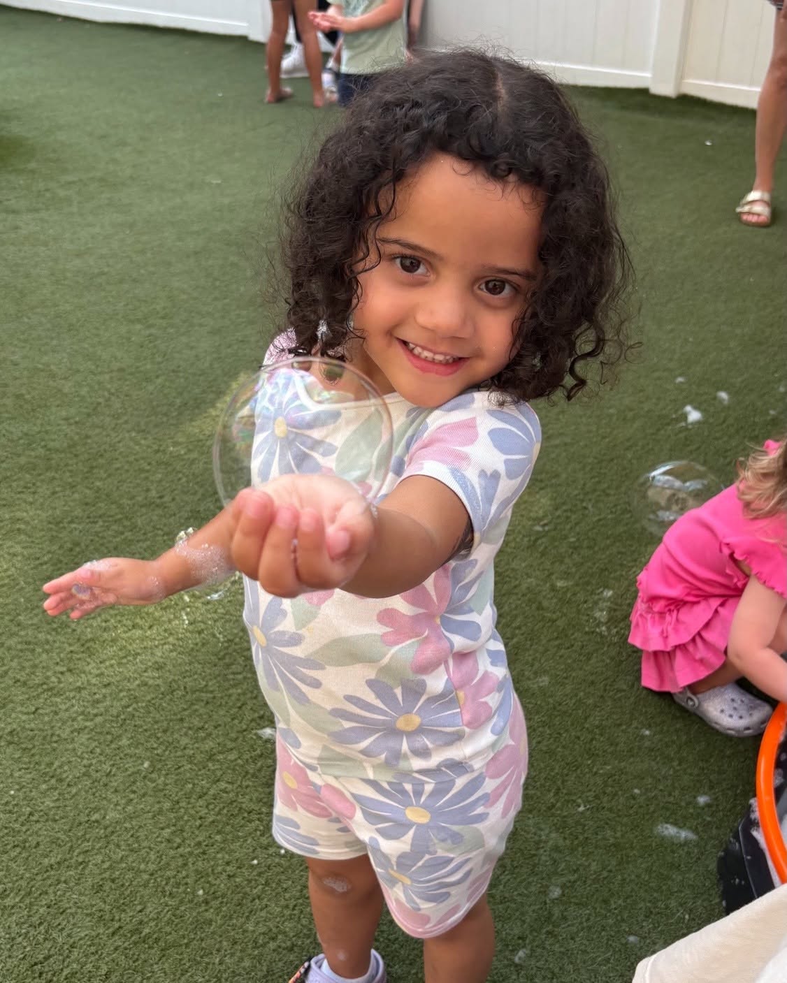 Child reaching out to touch a soap bubble on artificial grass