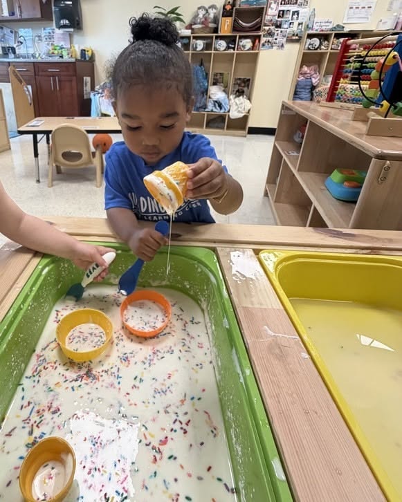 Child playing with colorful sprinkles and white liquid in a sensory table