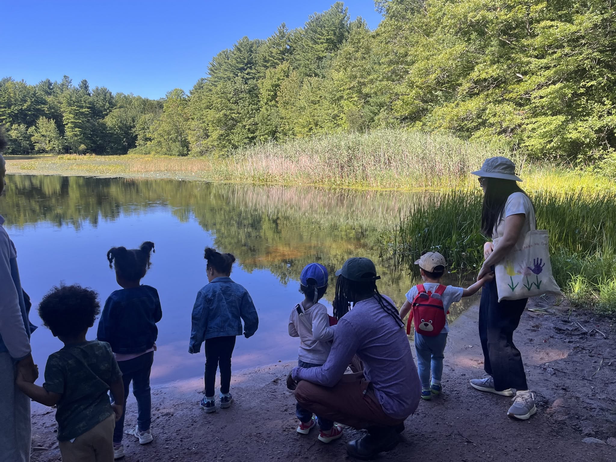 Group of children and adults standing on a muddy bank by a lake