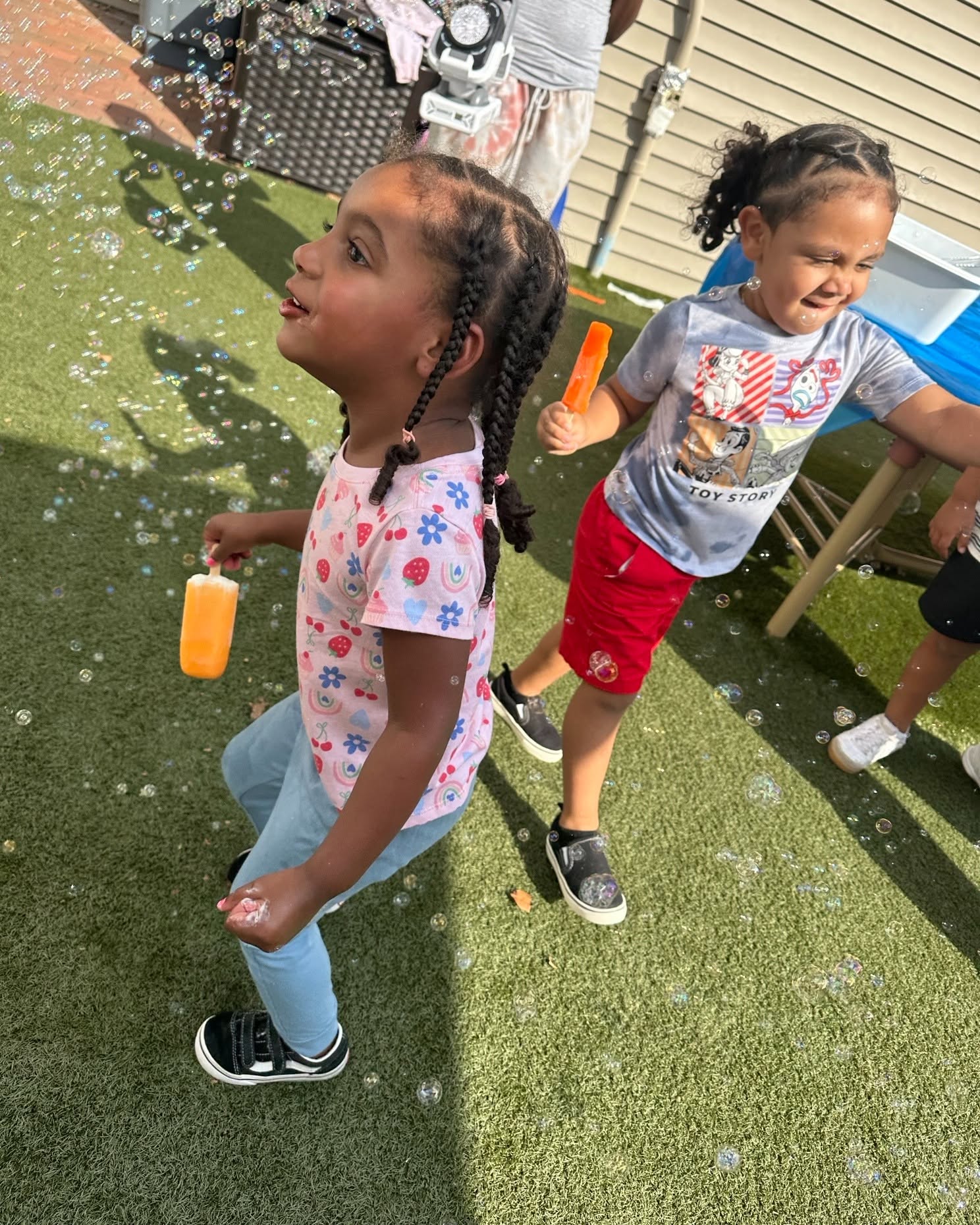 Two children playing with bubbles outdoors while holding popsicles