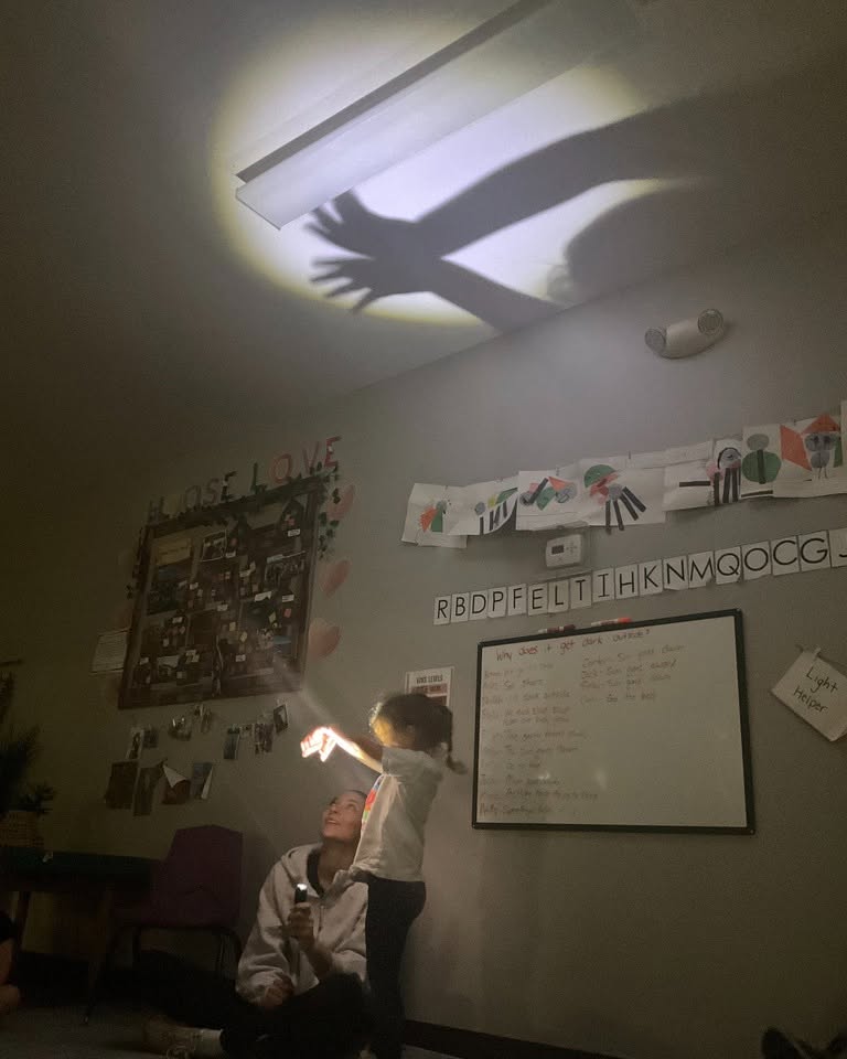 A person and a child casting shadow puppets on a ceiling with a flashlight