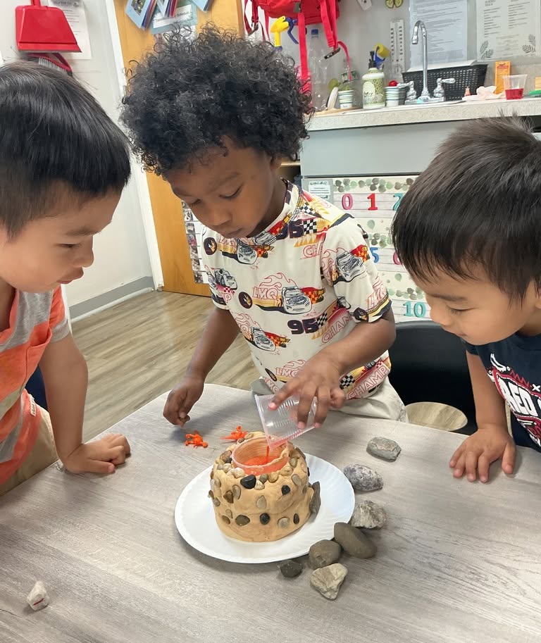 Three children observing a model volcano experiment at a table
