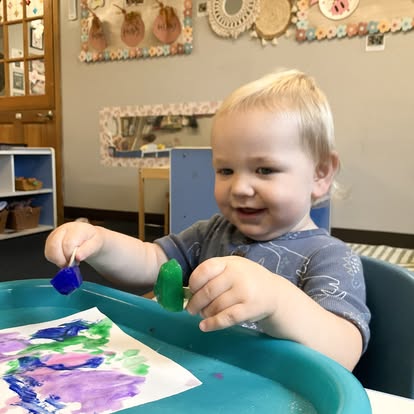 Child painting on paper using ice cubes in a classroom