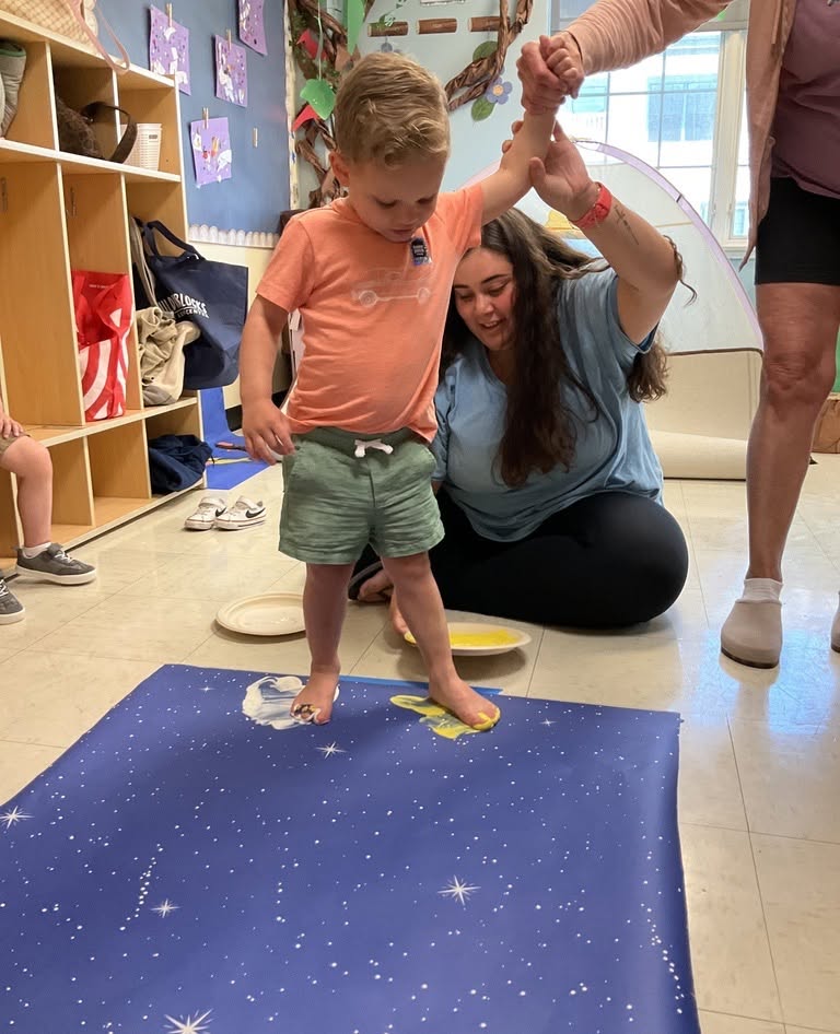 Child stepping in paint on a star-patterned mat with assistance