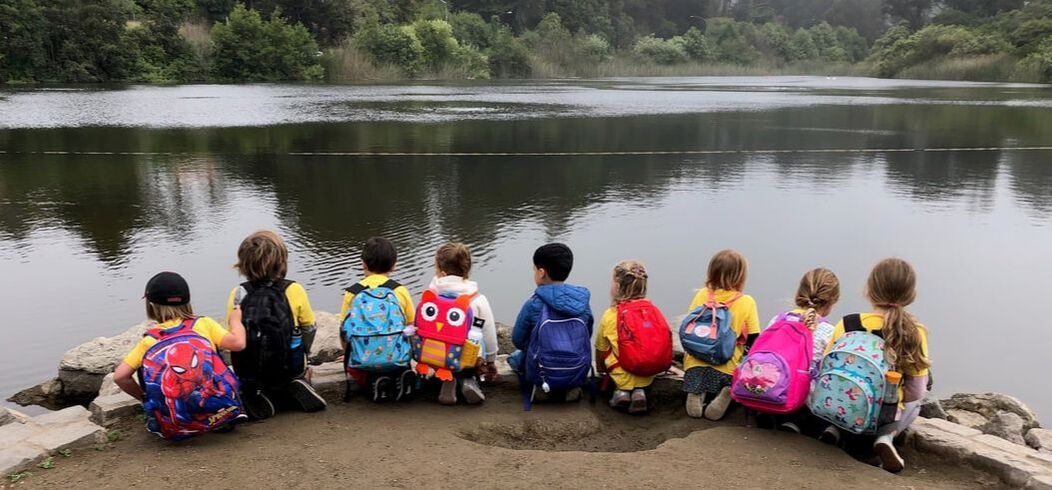 Children with backpacks sitting by a lake