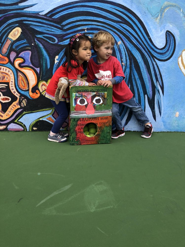 Two children standing next to a decorated box with tennis balls inside