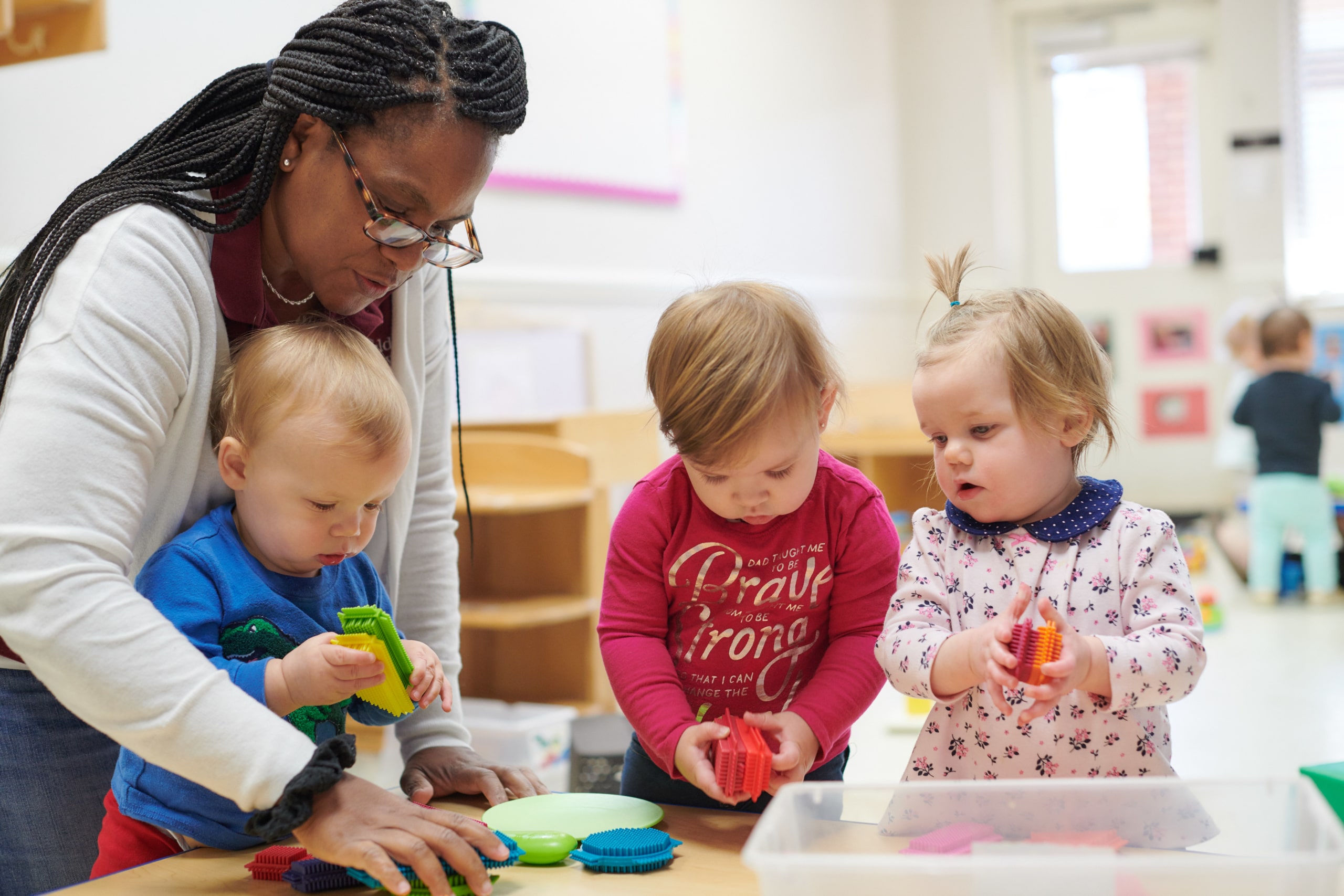 Adult and three children playing with toys in a classroom
