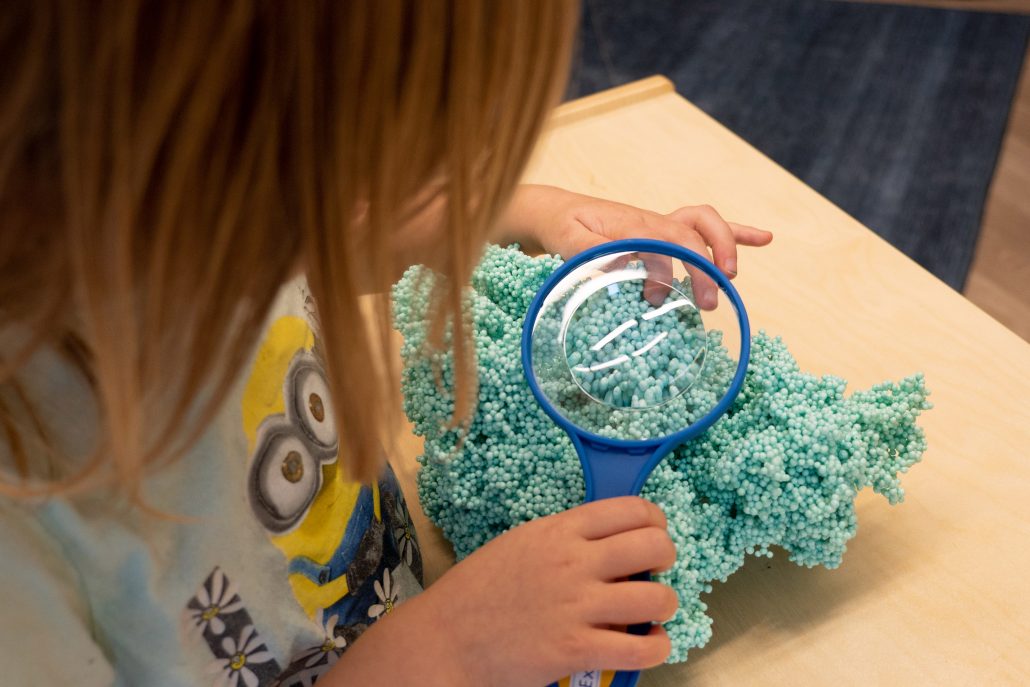 Child looking at kinetic sand through a magnifying glass