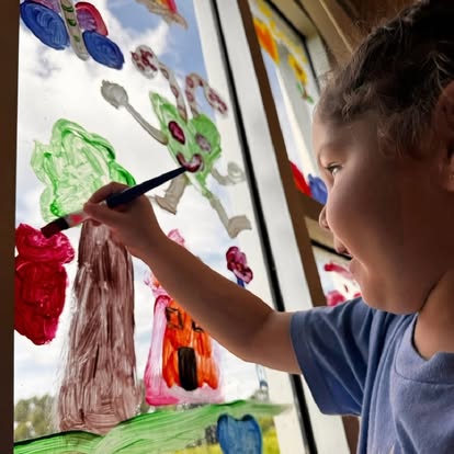 Child painting on a window with a paintbrush