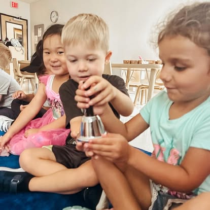 Three children playing with a bell in a classroom