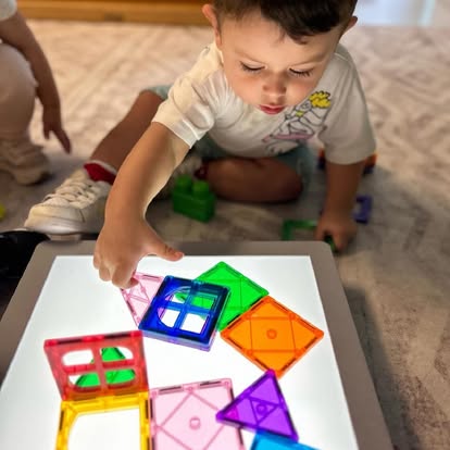Child playing with colorful magnetic tiles on a light table