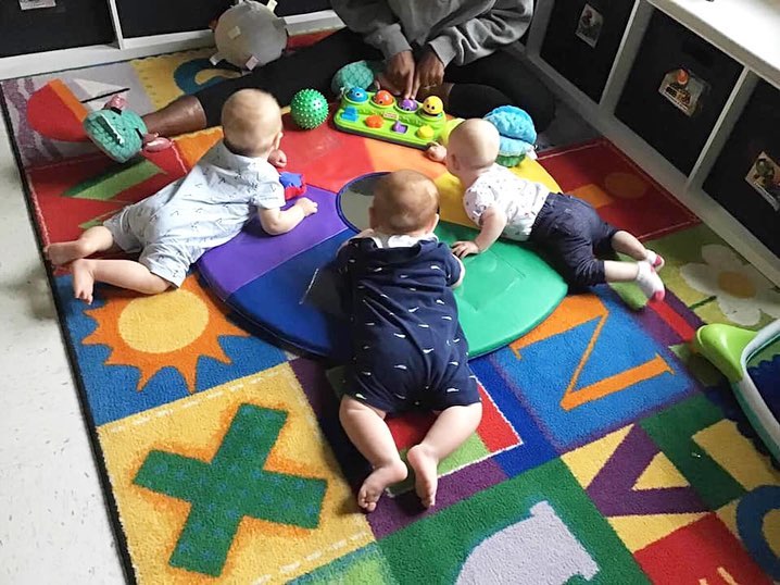 Person sitting on floor with three babies playing on a colorful rug