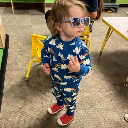 Child in blue rainbow pajamas and sunglasses standing indoors