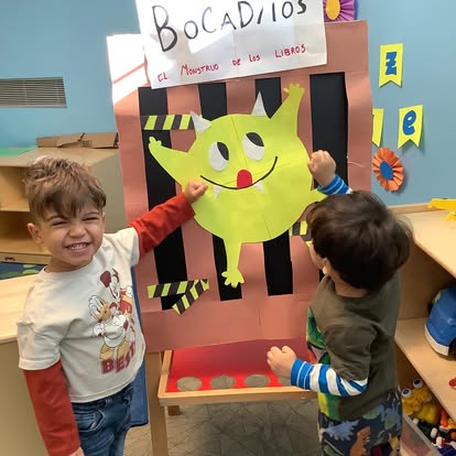 Two children interacting with a green monster cutout on an easel
