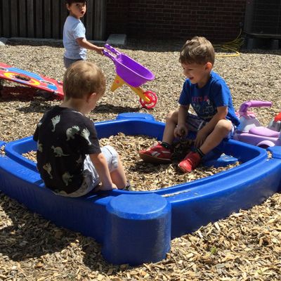 Three children playing in a sandbox with wood chips